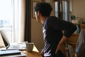 在宅ワークの30代男性が朝のデスクで片手を腰に添える様子